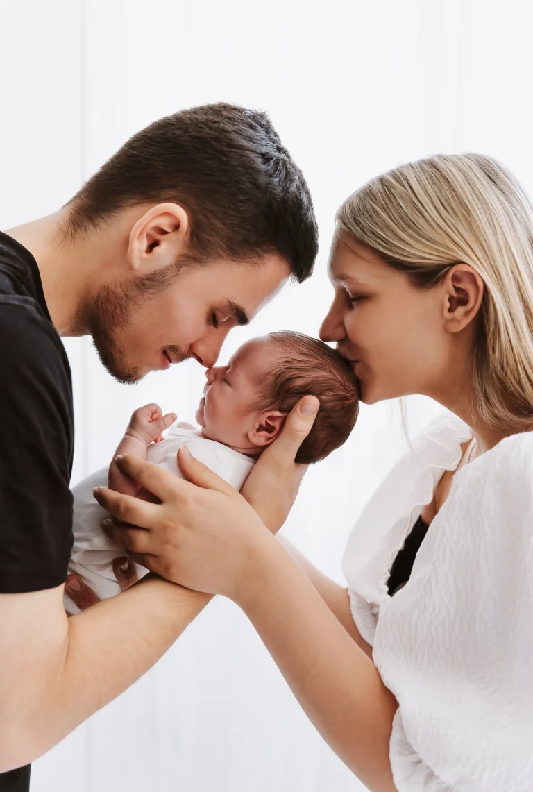 "Starša držita svojega novorojenčka v naročju, poljub na čelo."