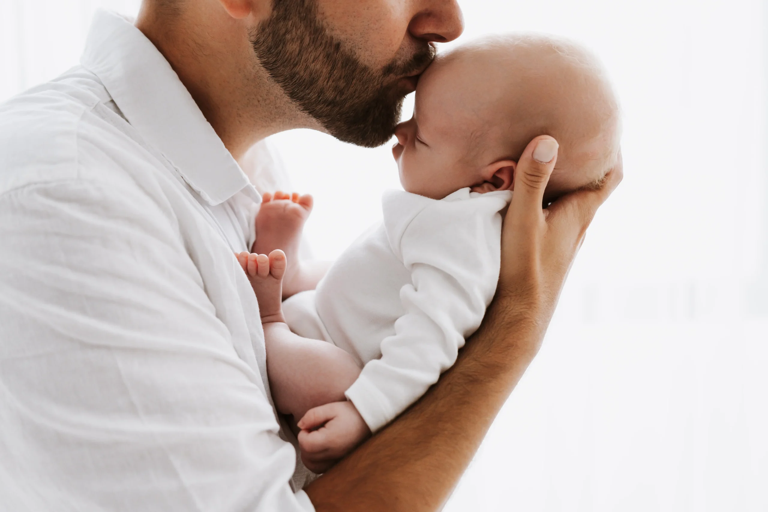 "Novorojenček v naročju staršev, nežno stisnjen ob očeta."