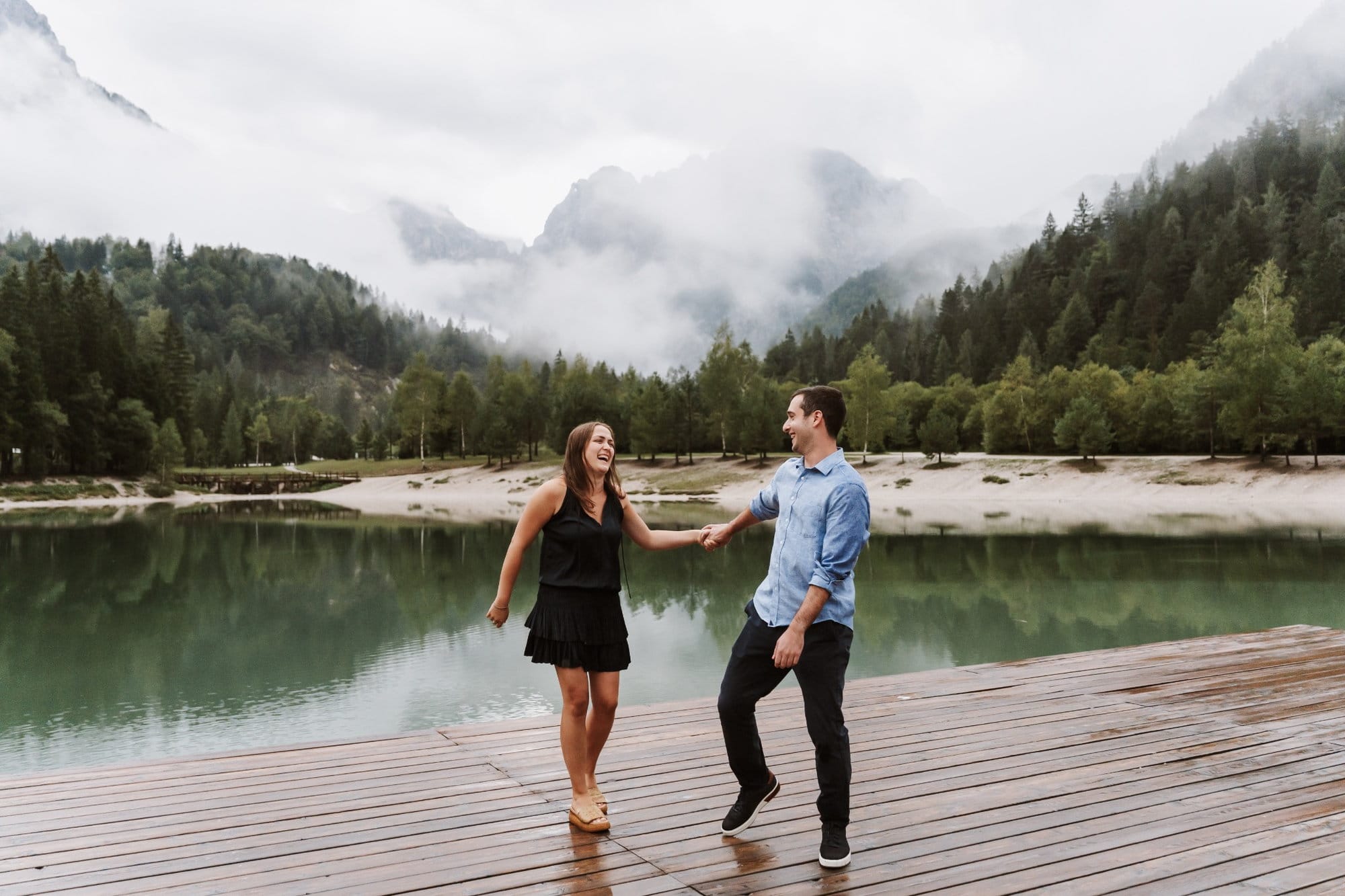 Laughing engaged couple at Lake Jasna with misty Julian Alps in the background