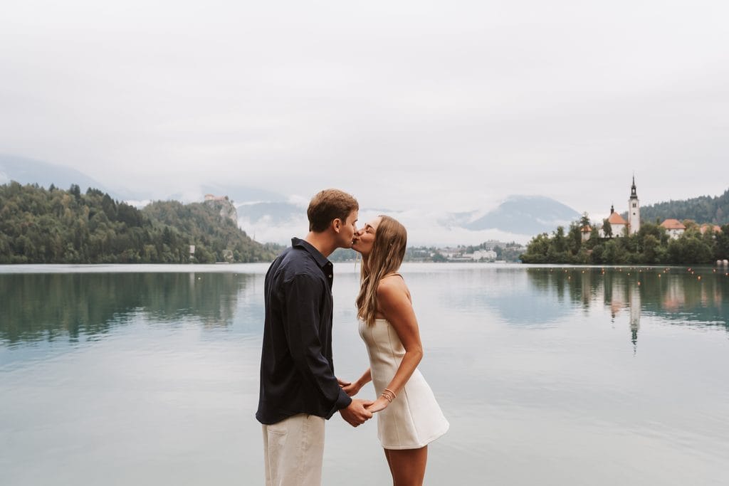 Couple kissing beside Lake Bled after their proposal, with the island church behind them